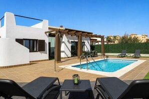 Ein moderner Poolbereich im Freien mit einer Pergola, Liegestühlen und einem Tisch mit Kerze.