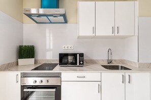 Une cuisine moderne avec des meubles blancs, une hotte en acier inoxydable, un four à micro-ondes, un évier doté d’un robinet contemporain et un four encastré.