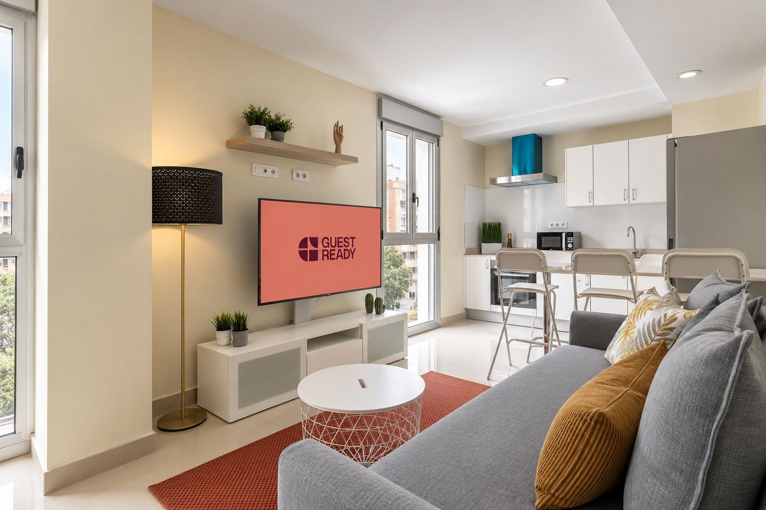 Una sala de estar moderna con un televisor de pantalla plana mostrando 'GUEST READY', un sofá, una mesa de centro y una alfombra roja.