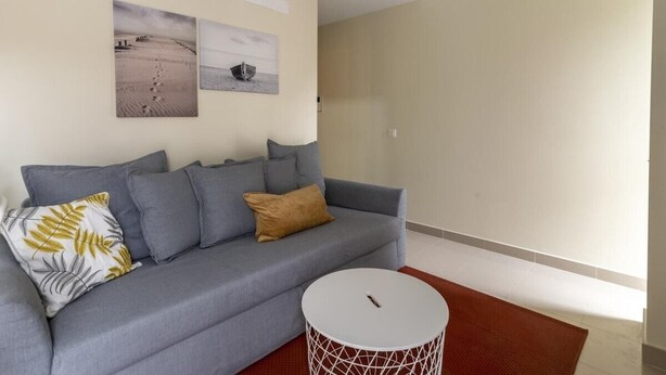 A modern living room with a grey sofa, a round coffee table, and two wall-mounted artworks. - GuestReady - 01C Livian Suites Ext 4 Pax (Las Palmas de Gran Canaria)