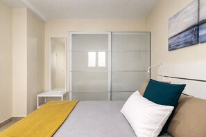 A bedroom with a bed, a bedside table, a wardrobe, and a painting on the wall. - GuestReady - 01C Livian Suites Ext 4 Pax (Las Palmas de Gran Canaria)
