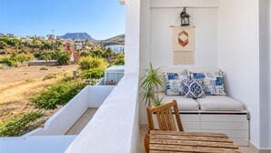 Ein Balkon mit Blick auf eine Hügelstadt, eine weiße Mauer mit einer hängenden Laterne und eine Couch mit gemusterten Kissen.
