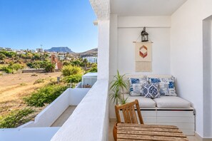 A balcony with a view of a hillside town, a white wall with a hanging lantern, and a sofa with patterned cushions. - GuestReady - La Palmita Agaete with Pool (Agaete)