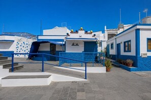 A coastal building with a blue and white facade, a staircase leading to the entrance, and potted plants on the ground.