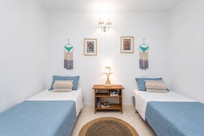 A room with two beds, a small wooden table, wall-mounted lamps, and decorative macramé hangings. - GuestReady - La Palmita Agaete with Pool (Agaete)