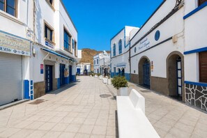 A narrow street with white buildings, blue doors, and signage for shops and services. - GuestReady - La Palmita Agaete with Pool (Agaete)
