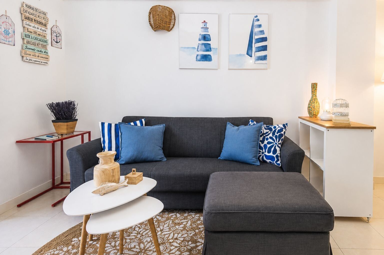 Una sala moderna con un sofá gris, cojines azules, una mesa de centro blanca y una mesita de noche con una planta.