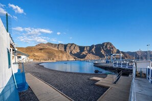 A coastal marina with a rocky shoreline, a wooden jetty, and a mountainous backdrop. - GuestReady - La Palmita Agaete with Pool (Agaete)