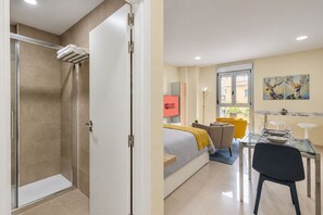 Habitación de hotel con ducha, cama, zona de estar y comedor.