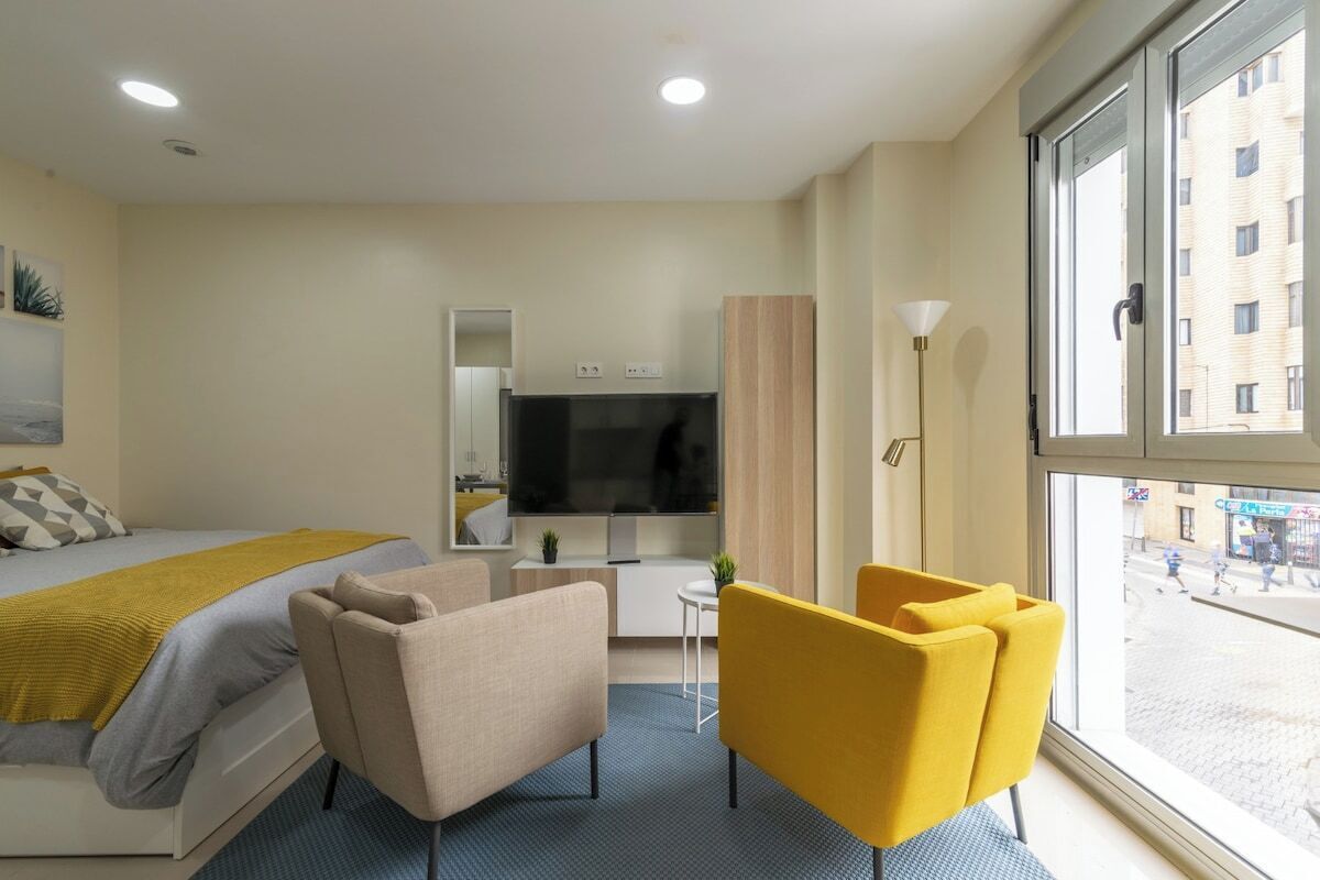 A hotel room with a bed, a TV, a desk, a chair, and a large window.