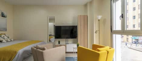 A hotel room with a bed, a TV, a desk, a chair, and a large window.