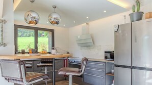 A modern kitchen with bar stools, a stainless steel refrigerator, and a window with a view of greenery.