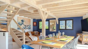 A modern interior with a wooden staircase, a dining area with a table set for four, and a sofa in the living area.