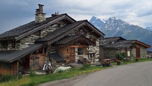 A stone building with a wooden facade, a sign indicating a restaurant, and a view of snow-capped mountains in the background.