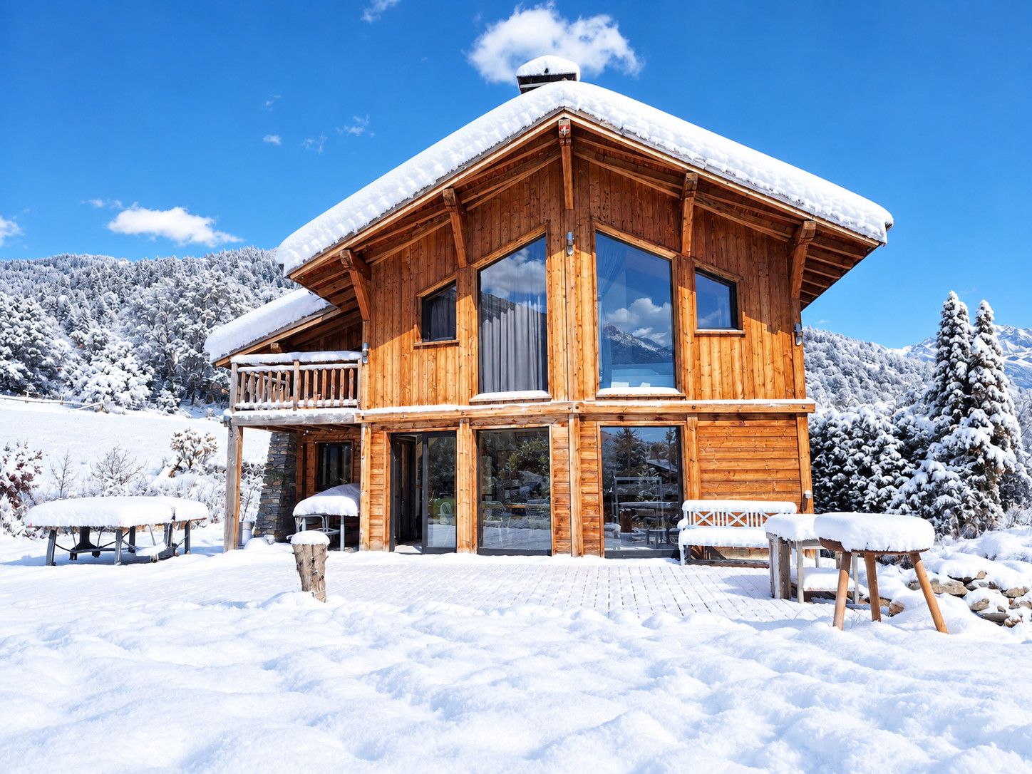 A wooden chalet with a balcony, large windows, and a snowy landscape in the background.