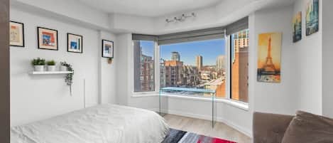 A bedroom with a large window, a bed, a sofa, and a city view.