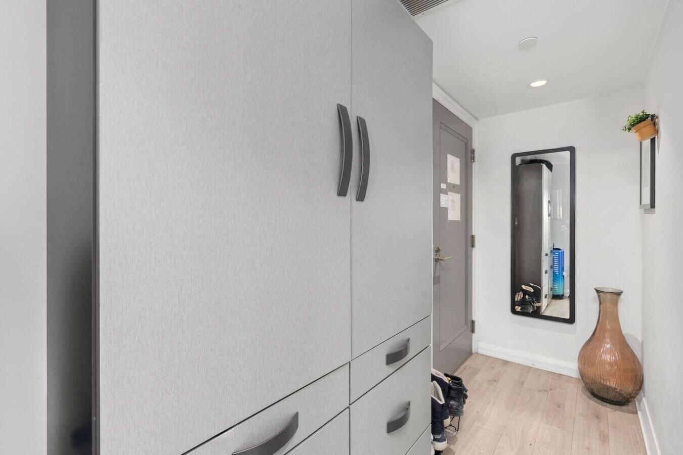 A hallway with grey wardrobe, a mirror, a vase, and a door.