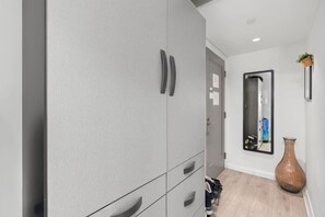 Un couloir avec une armoire grise, un miroir, un vase et une porte.