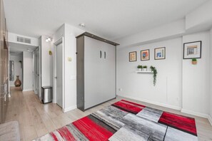 Ein modernes Interieur mit einem Flur, der zu einem Zimmer führt, einem rot-grauen StreifenTeppich und gerahmten Bildern an der Wand.
