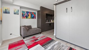 Uma sala de estar moderna com um sofá, um quadro abstrato colorido e uma área de cozinha com armários e bancada.