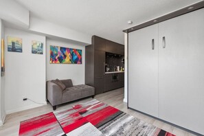 Ein modernes Wohnzimmer mit einer Couch, einem farbenfrohen abstrakten Gemälde und einer Küchenzeile mit Schränken und Arbeitsplatte.