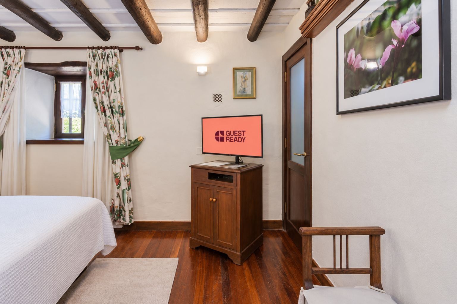 Une chambre d’hôtel avec un lit, une armoire en bois portant une pancarte, un tableau encadré et une fenêtre avec des rideaux.