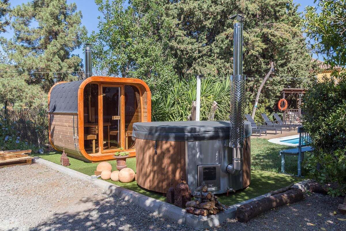 A wooden cabin with a glass door, a hot tub, and a pool area surrounded by trees.