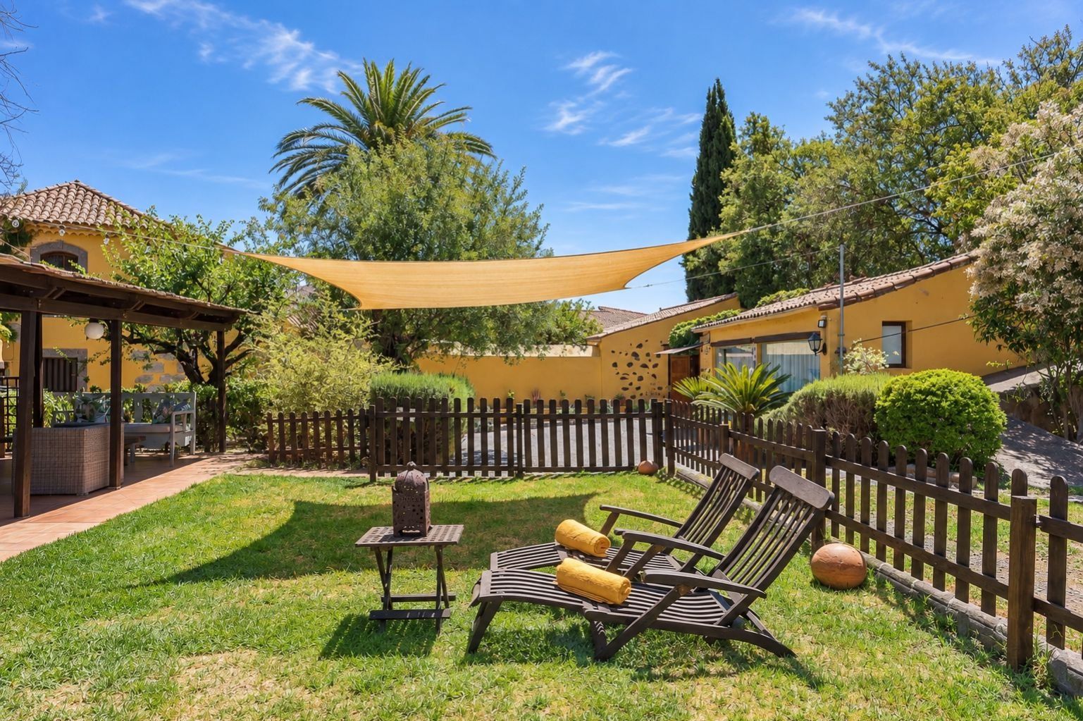 Un patio exterior soleado con cerco de madera, una zona con sombra y un conjunto de asientos.