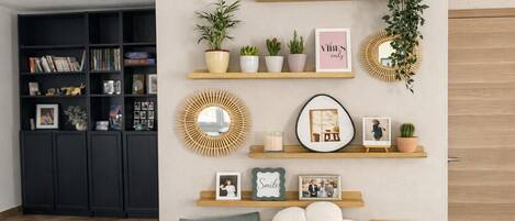A room with a bookshelf, wall-mounted shelves with decorative items, a mirror, and a large flower-shaped cushion.