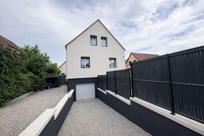 A modern two-story house with a garage, a gravel driveway, and a black metal fence. - Villa Bartholdi – House & Garden in Holtzheim (Holtzheim)