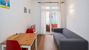 Un ambiente compatto con un tavolo da pranzo in legno, sedie rosse, un divano grigio e una piccola TV.