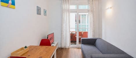 A compact living space with a wooden dining table, red chairs, a grey sofa, and a small TV.