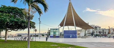 Una plaza pública con un pabellón moderno, una parada de autobús y un jardín de flores.