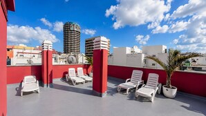 Una terrazza sul tetto con poltrone da relax bianche, pilastri rossi e vista sugli edifici della città.