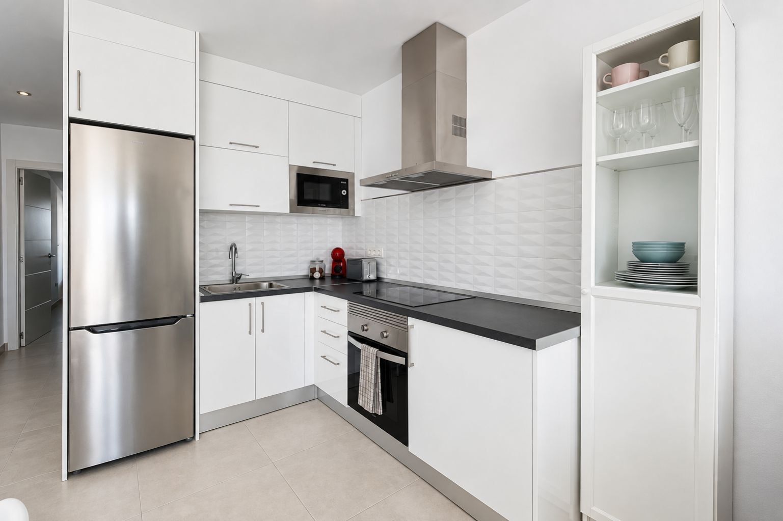 A modern kitchen with stainless steel appliances, white cabinetry, and a black countertop.