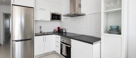 A modern kitchen with stainless steel appliances, white cabinetry, and a black countertop.