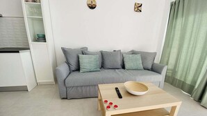 A modern living room with a grey sofa, a wooden coffee table, and a kitchen area with white cabinetry. - GuestReady - Senator Terrace Retreat (Costa Teguise)