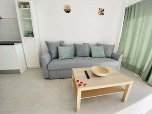 Ein modernes Wohnzimmer mit grauem Sofa, einem Holztisch und einer Küchenzeile mit weißen Schränken.