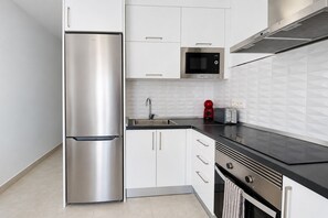 A modern kitchen with stainless steel appliances, white cabinetry, and a black countertop. - GuestReady - Senator Terrace Retreat (Costa Teguise)