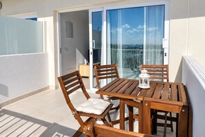 A wooden table and chairs on a balcony with a glass door leading to a pool area. - GuestReady - Senator Terrace Retreat (Costa Teguise)