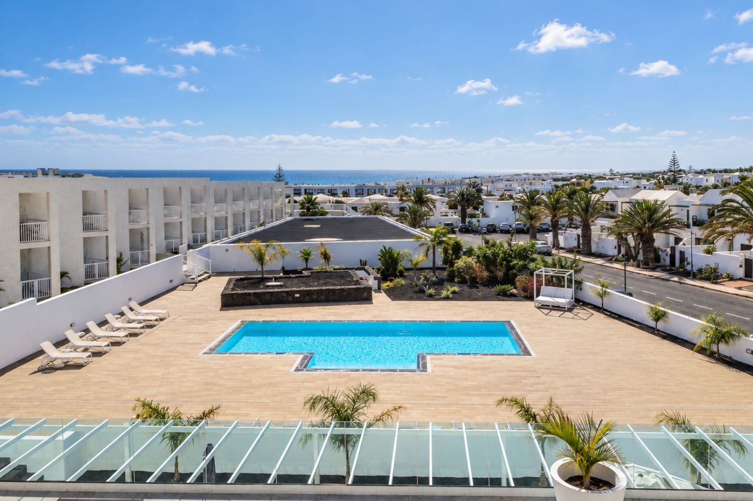 Zona d'una piscina al terrat amb gandules, una piscina i vistes al mar i edificis.