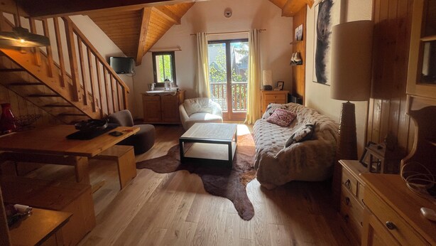 L’intérieur d’un chalet accueillant, avec un escalier en bois, un canapé, une table et une grande fenêtre.