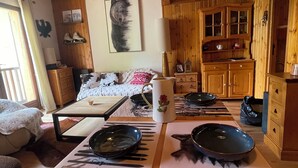 L’intérieur chaleureux d’un chalet avec un plafond en bois, une table à manger avec de l’assiette, un canapé et un coin cuisine.