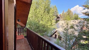 Un balcon en bois offrant une vue sur une zone boisée et sur un bâtiment doté d’un toit en pente.