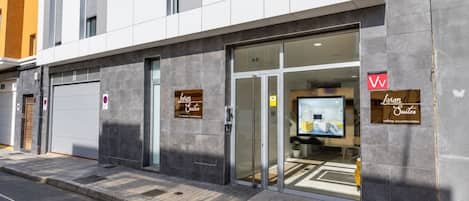 A modern hotel entrance with a glass door, a digital display showing a room, and signage for 'Liven Suites' and 'holiday accommodation'.