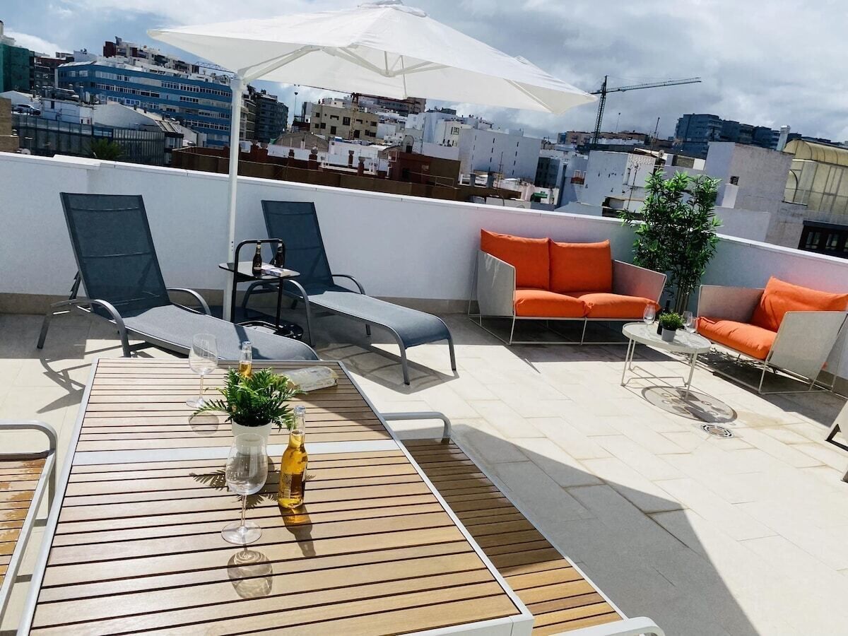A rooftop terrace with outdoor seating, a table with drinks, and a view of the cityscape.