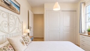 Een slaapkamer met een bed, nachtkastje, lamp, kapstok en een deur.