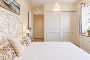 A bedroom with a bed, a nightstand, a lamp, a dresser, and a door. - GuestReady - Bright Stay with Balcony (Caleta de Fuste)