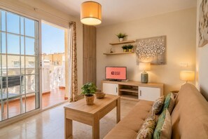 A modern living room with a sofa, a coffee table, a TV, and a balcony with a view. - GuestReady - Bright Stay with Balcony (Caleta de Fuste)