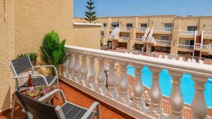 Een balkon met een zwembad, stoelen en een plant in een pot.
